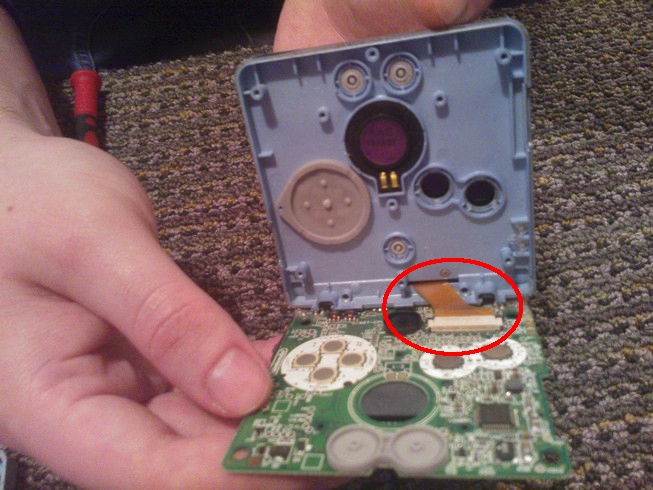 Laying the board down revealing a circled ribbon cable and connector